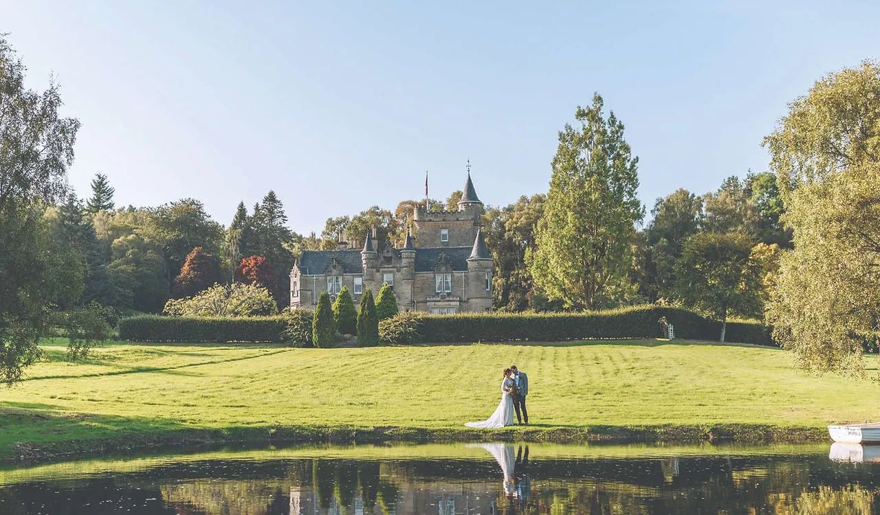 Bride and groom by a tranquil lochan with Rothes Glen castle in the distance.