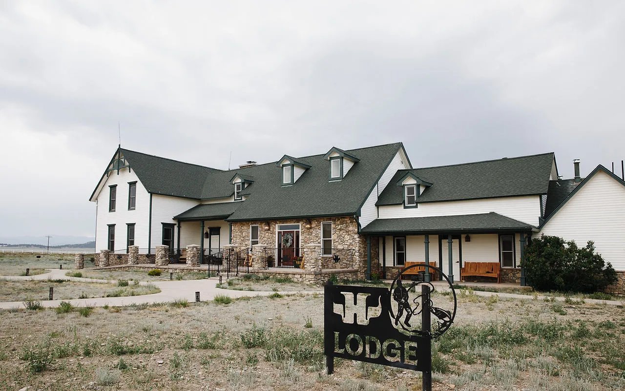 White main lodge building with a green roof and stone facade under a cloudy sky.