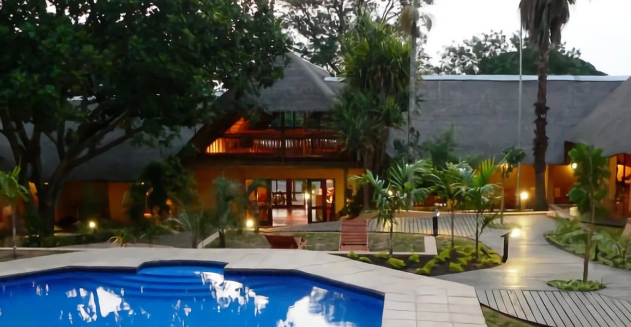 Thatched-roof lodge building with a wooden balcony, nestled among dense greenery