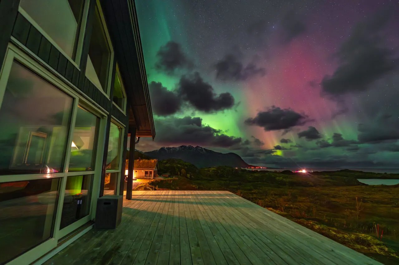 Lodge exterior with large windows under a vibrant green and pink aurora