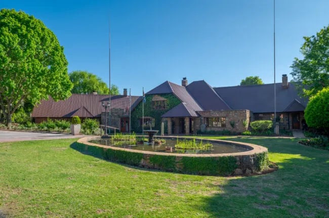 Grand lodge entrance with a paved driveway, manicured lawns, and mature trees