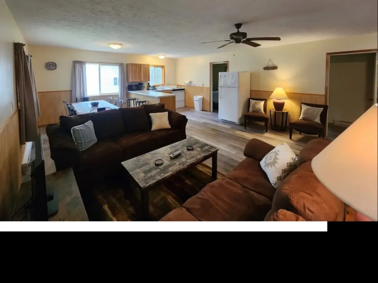 Open-concept living room and kitchen with dark sofas and wood paneling