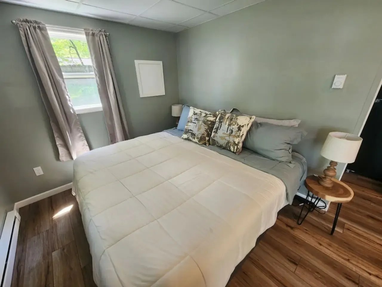 Serene bedroom with a queen bed, light green walls, and wood-look flooring