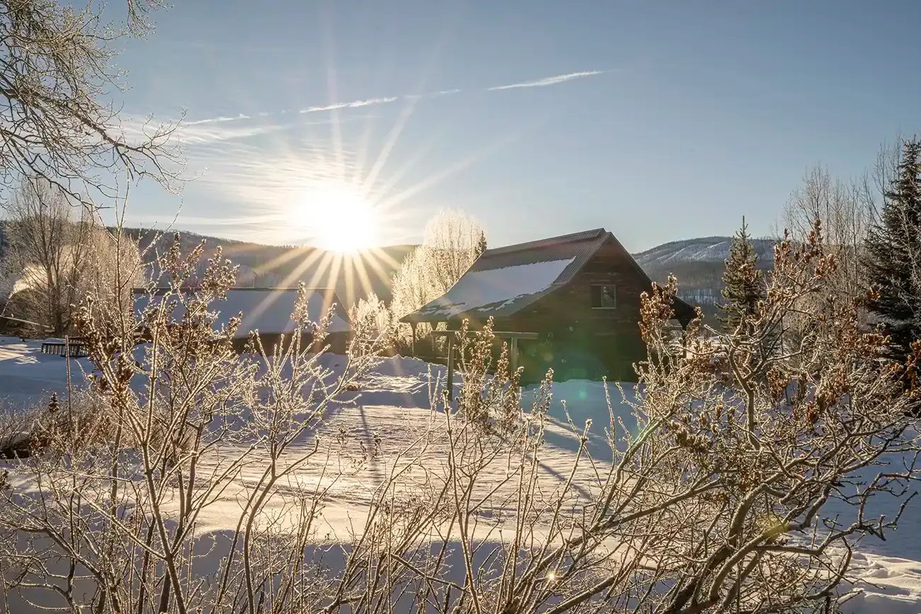 Snow-covered cabin with a bright sunburst over the roof in winter