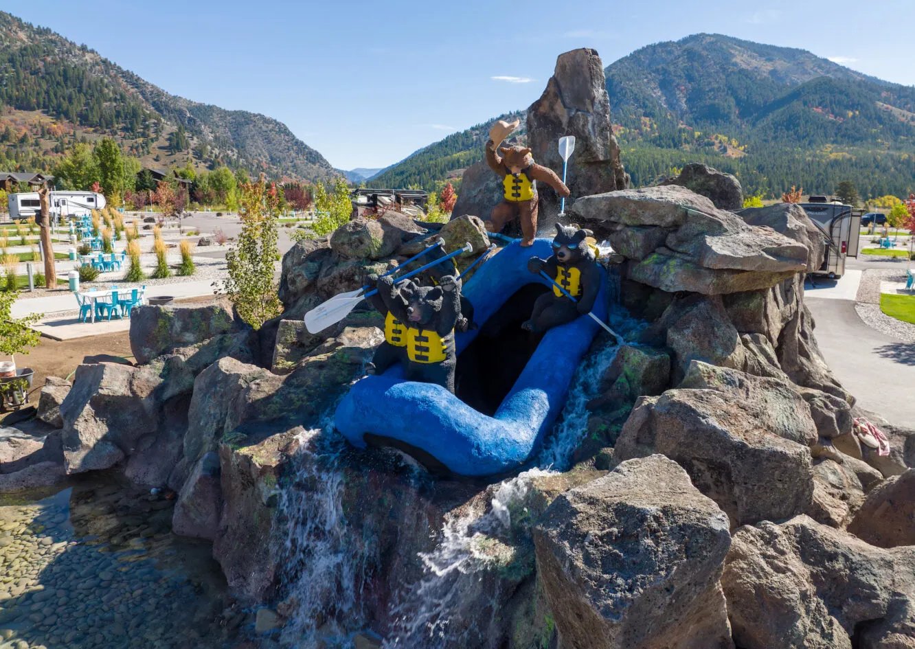 Rock formation with a blue rafting sculpture and people, set in a sunny mountain landscape