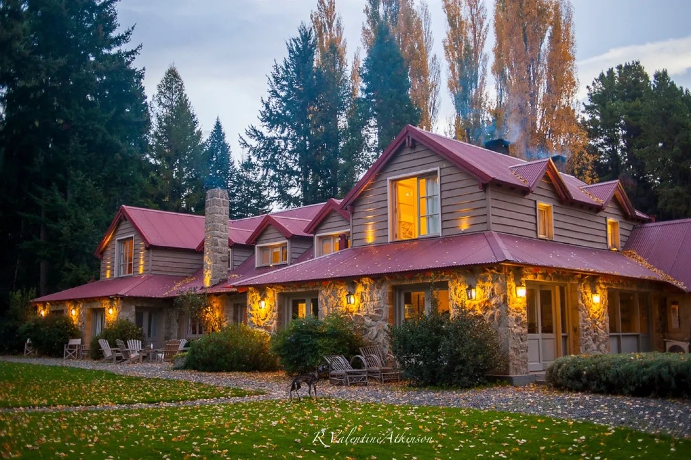 Lodge building illuminated at dusk, with a red roof and tall trees in the background