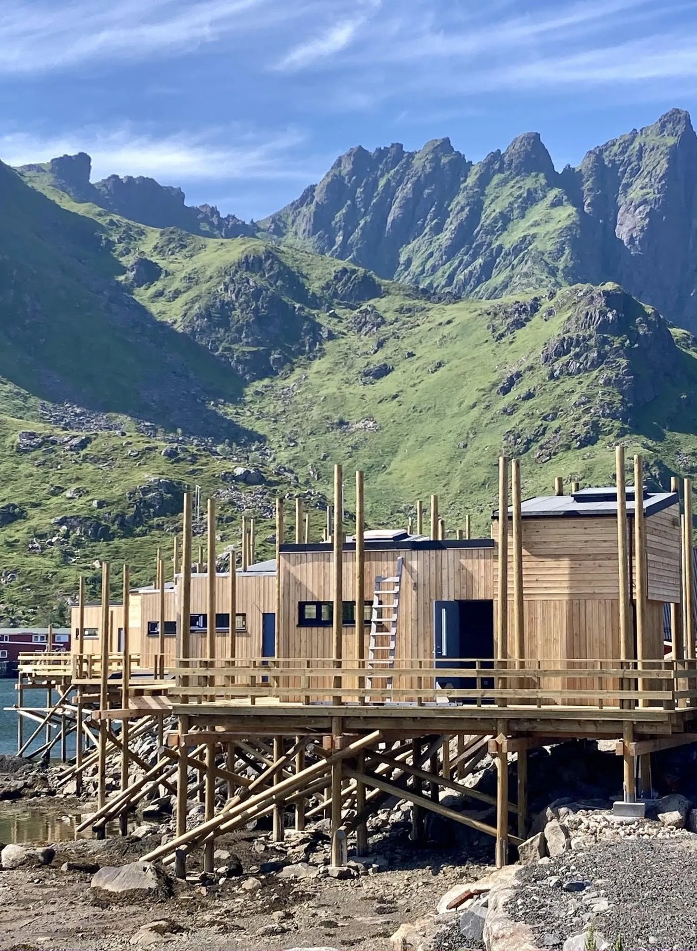 Modern wooden building exterior with a steep, sunlit mountain rising directly behind it