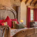 Guest bedroom with a rustic wooden bed frame, red pillows, and wood-paneled walls.