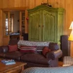 Cozy living area with a brown leather sofa, green antique cabinet, and wood-paneled walls.