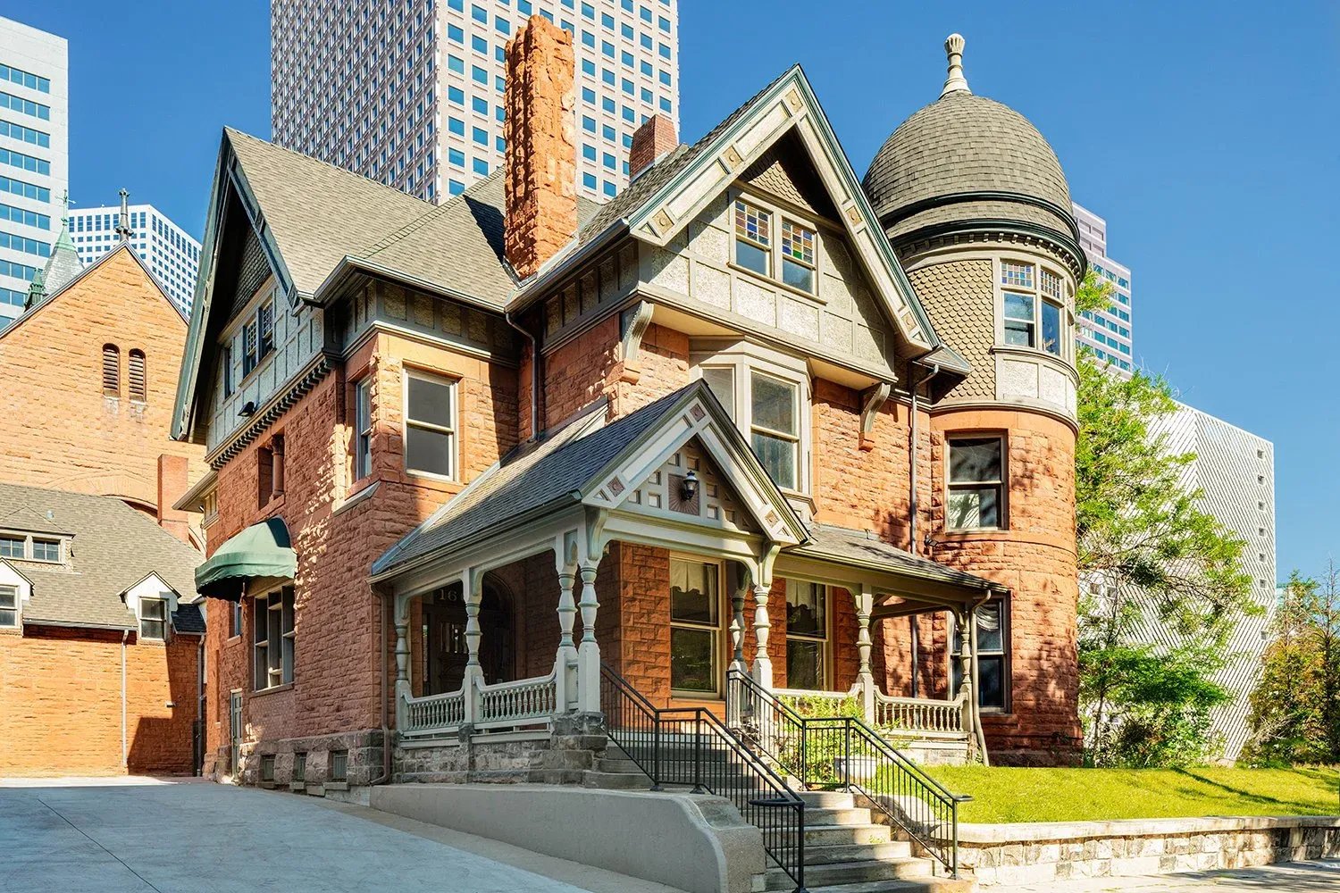 Ornate Victorian-style house with a turret and prickly pear cactus in the foreground on a sunny day.