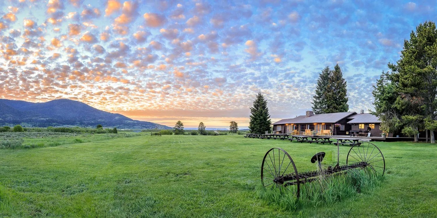 Lodge building in a green field at sunrise with a cloudy sky and distant mountains.