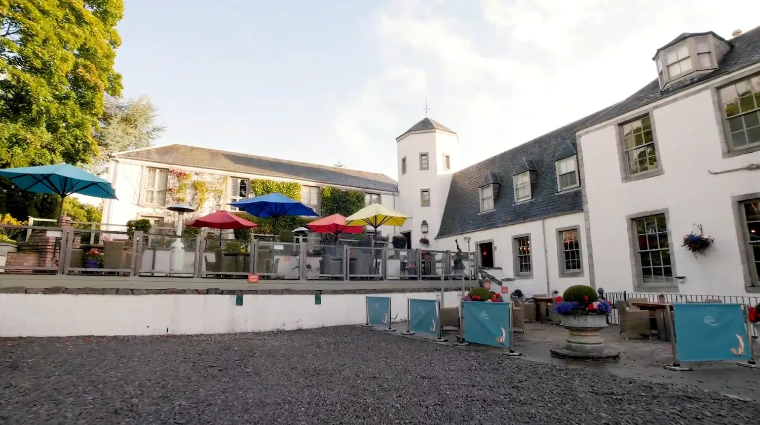 White lodge building exterior with an outdoor patio, colorful umbrellas, and lush trees