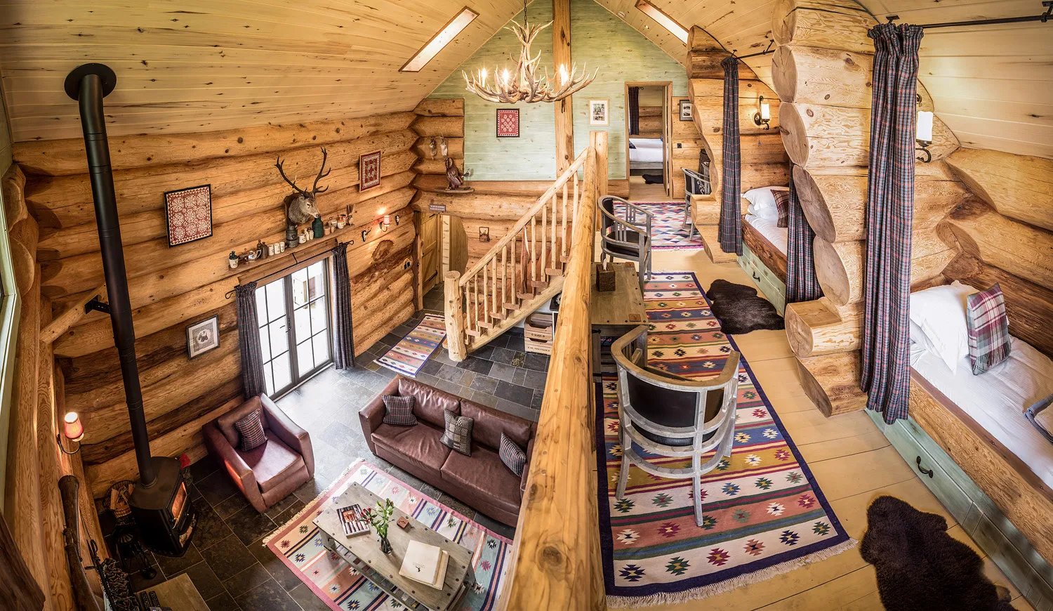 Log cabin interior with a living area, wood stove, and loft bedrooms