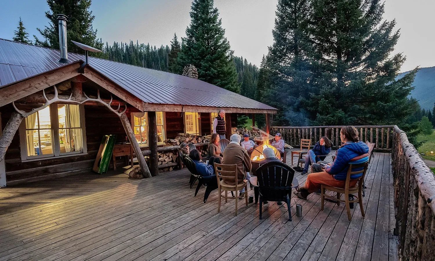 Guests gathered around a crackling campfire on the lodge's spacious wooden deck at dusk.