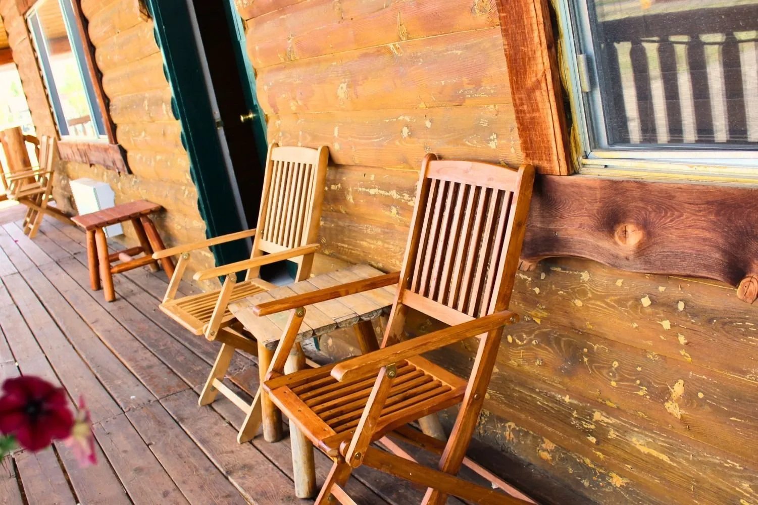 Wooden Adirondack chairs on a log cabin porch with a small side table