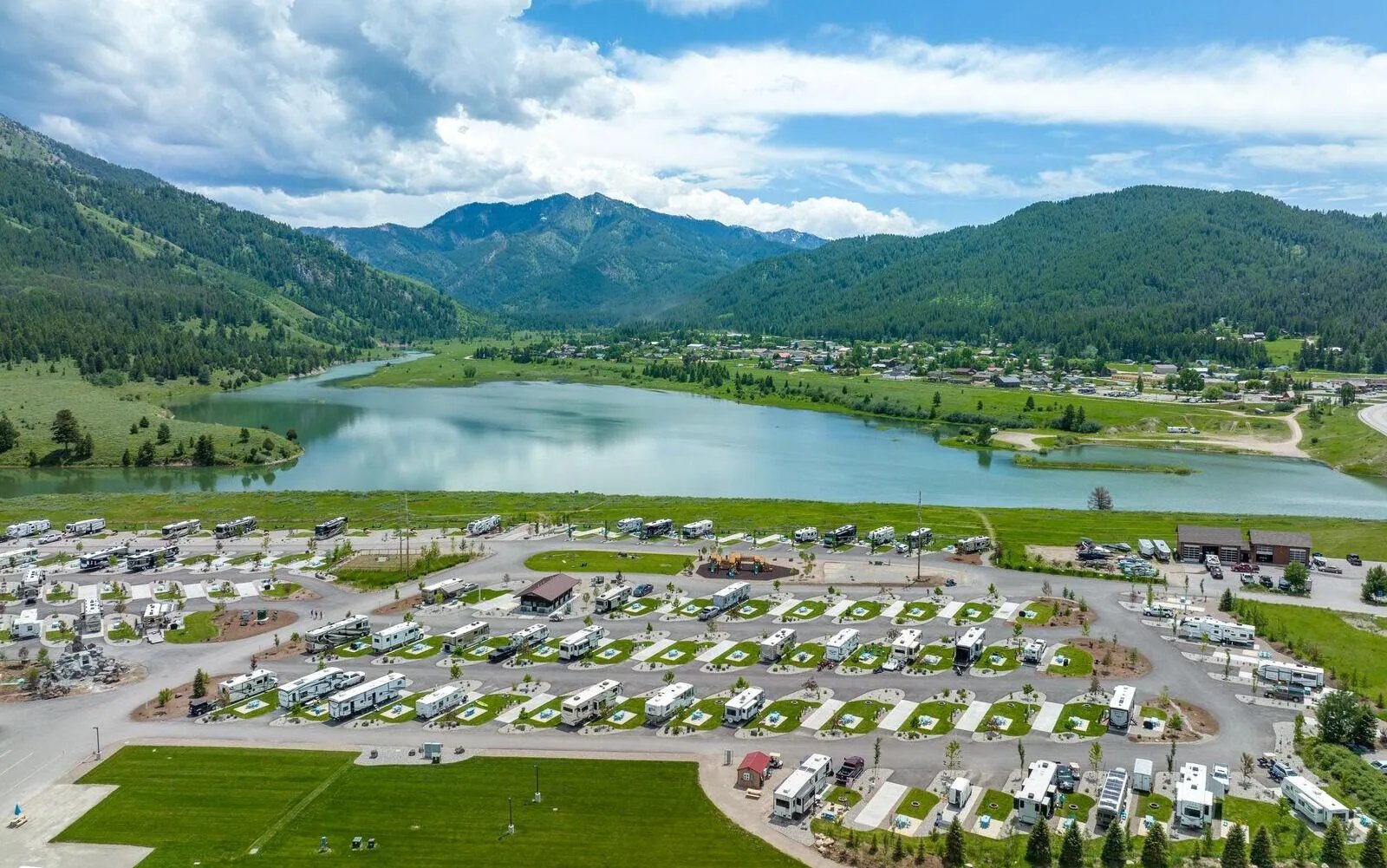 Aerial view of Alpine Valley RV Resort with RVs, a lake, and mountains under a blue sky