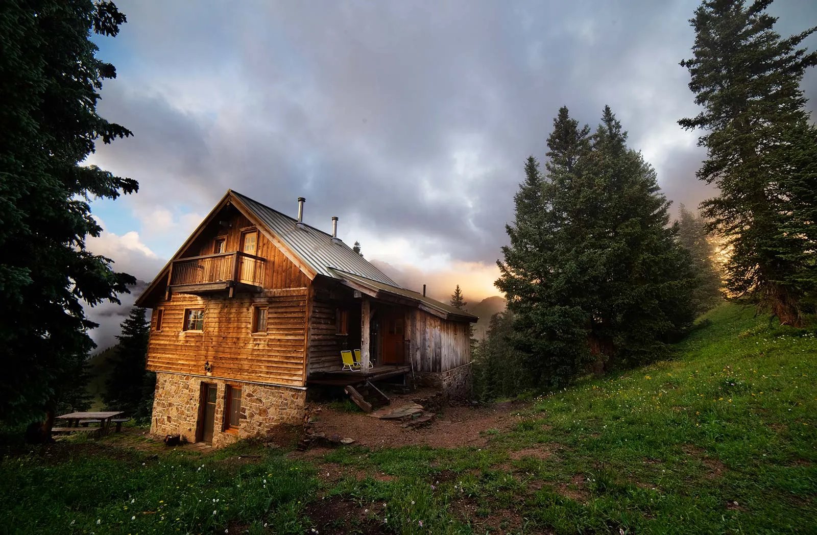 Rustic wooden hut nestled among pine trees on a summer evening.
