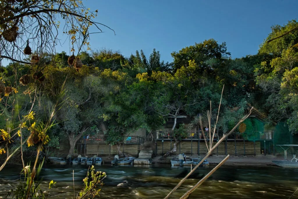 Aerial view of the Chobe River at sunset, surrounded by lush green and autumn-colored trees.