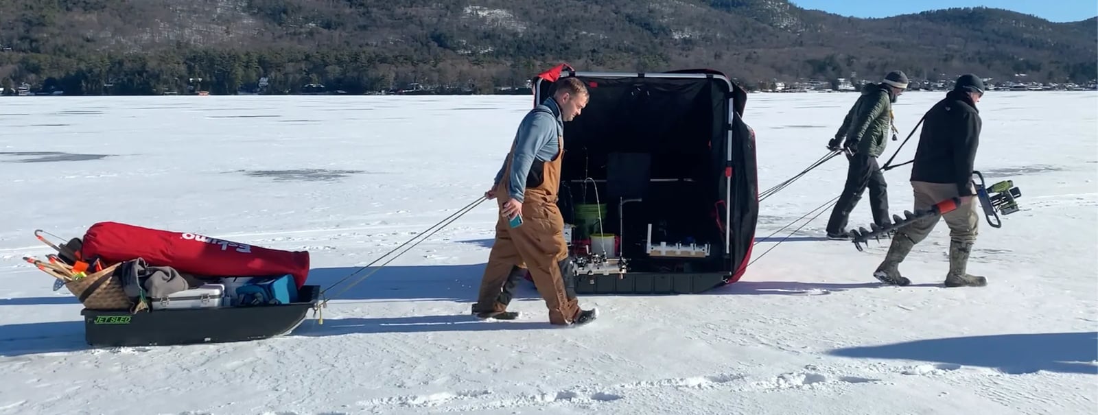 Man in a striped hat and sunglasses holding a Northern Pike on a sunny, snowy lake