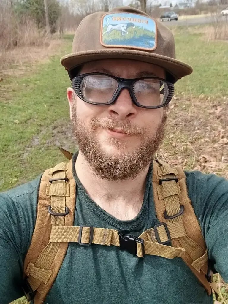 Man with a beard, glasses, and a cap smiling at the camera.