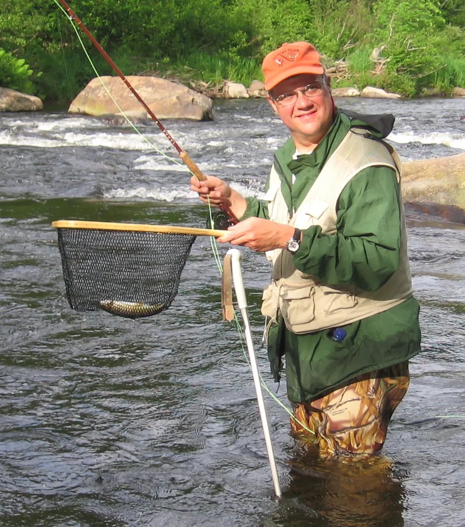 Man in waders holding a net with a Brown Trout in a river