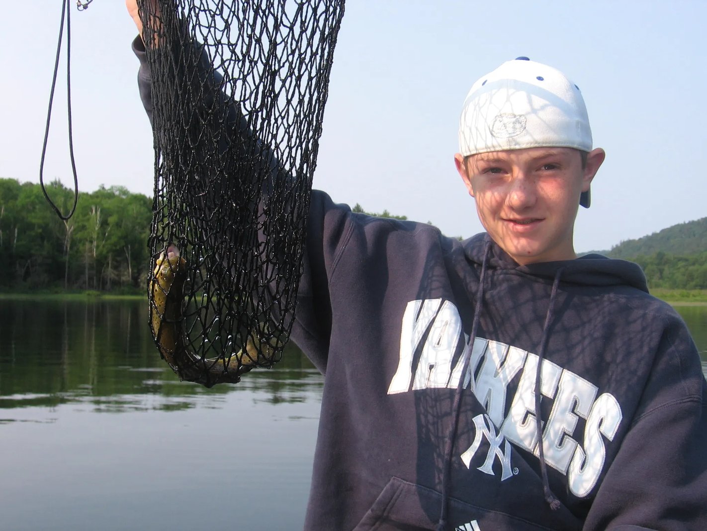 Young man holding a fish in a net on a lake