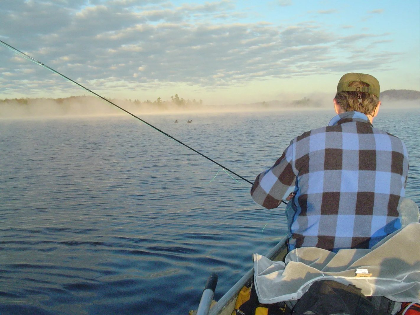 Angler in a green rain jacket holding a Brown Trout on a misty lake