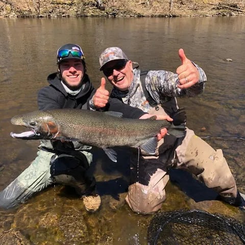 Two anglers in waders giving thumbs up, holding a large Steelhead in a river