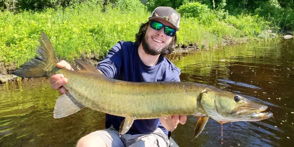 Man holding two Smallmouth Bass against a cloudy sky