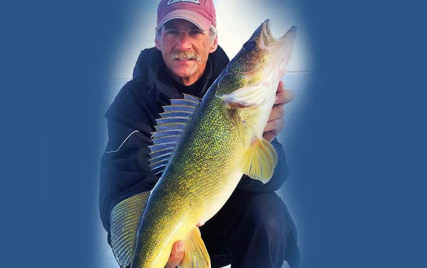 Man in a red cap smiling, holding a large walleye.