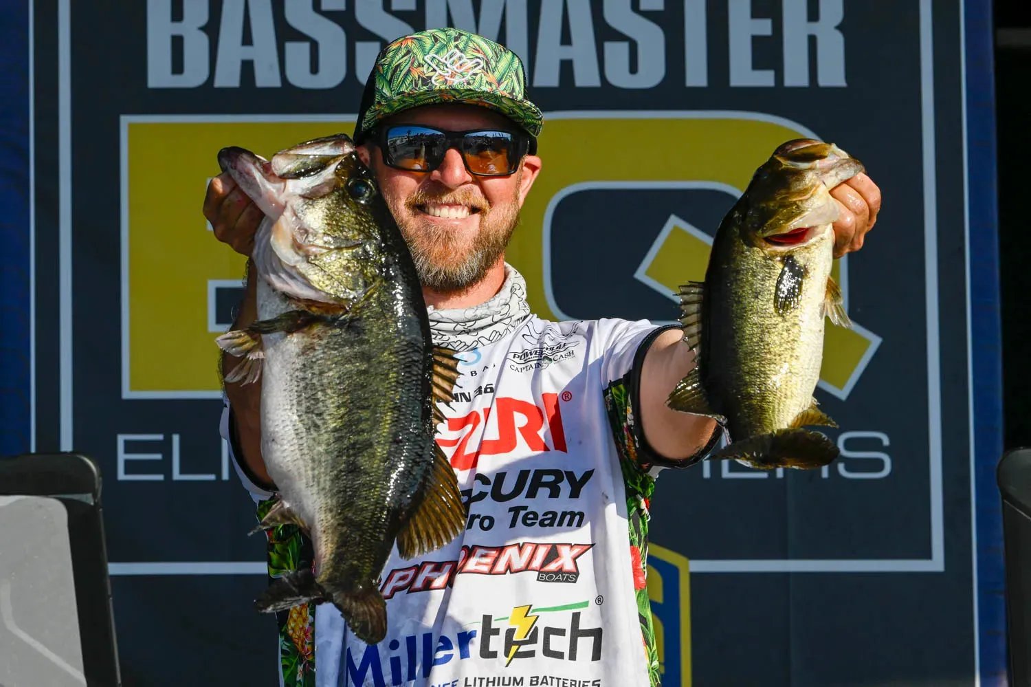 Angler in a blue shirt holding a Largemouth Bass in a bass boat.