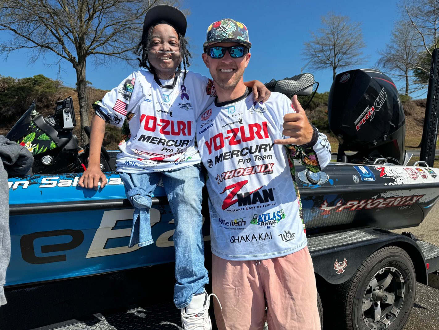 Smiling angler holding a large Largemouth Bass with a lure in its mouth.