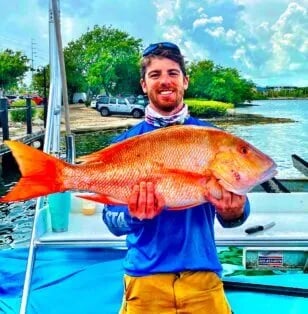 Smiling angler holding a large Red Snapper on a boat