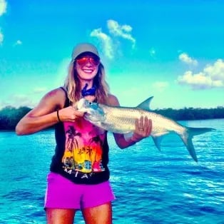 Woman smiling, holding a Tarpon over blue water