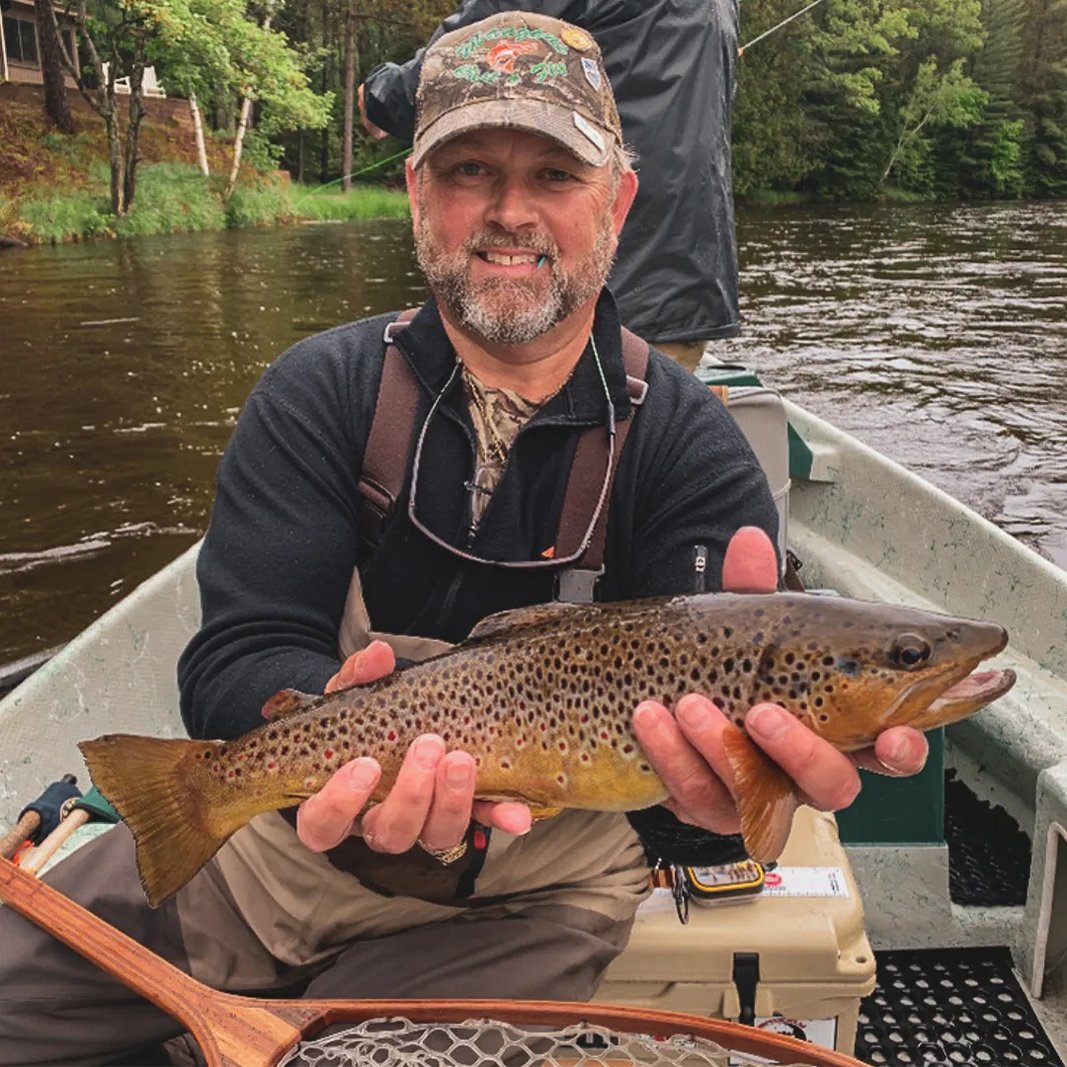 Man in a boat holding a spotted Brown Trout with a net visible.