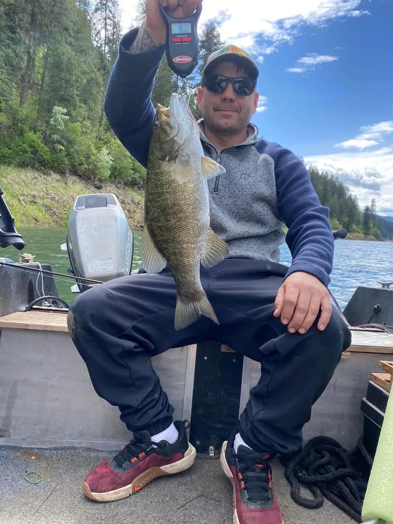 Man in a plaid shirt holding a large Smallmouth Bass on a boat.