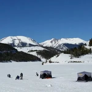 Ice fishing tents scattered across a snowy lake with snow-capped mountains in the background