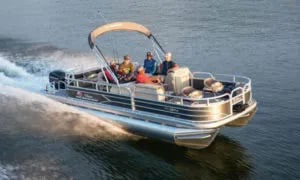 Pontoon boat with several people on board, cruising on calm water, leaving a wake