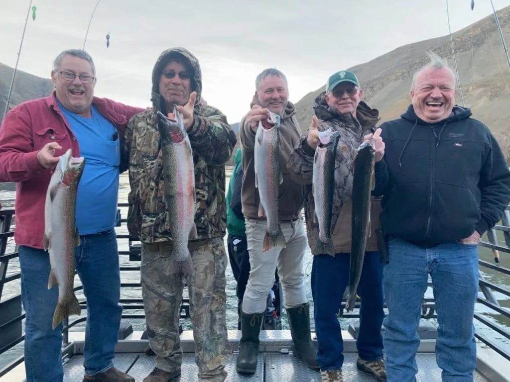 Five anglers on a boat deck smiling and holding their Rainbow Trout catches