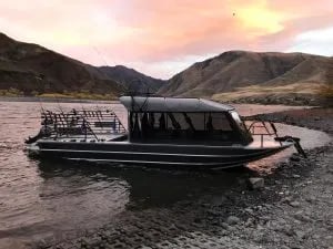Fishing jet boat beached on a riverbank at sunset with mountains in the background