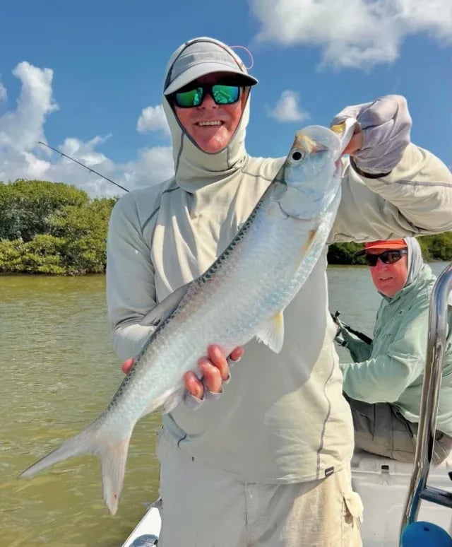 Angler holding a Tarpon on a boat in a mangrove channel.