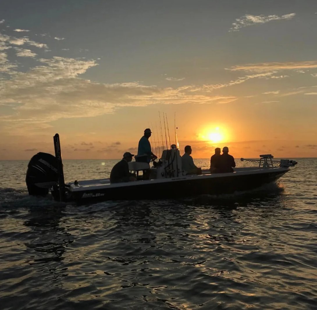 Silhouetted boat with anglers on the water at sunset.