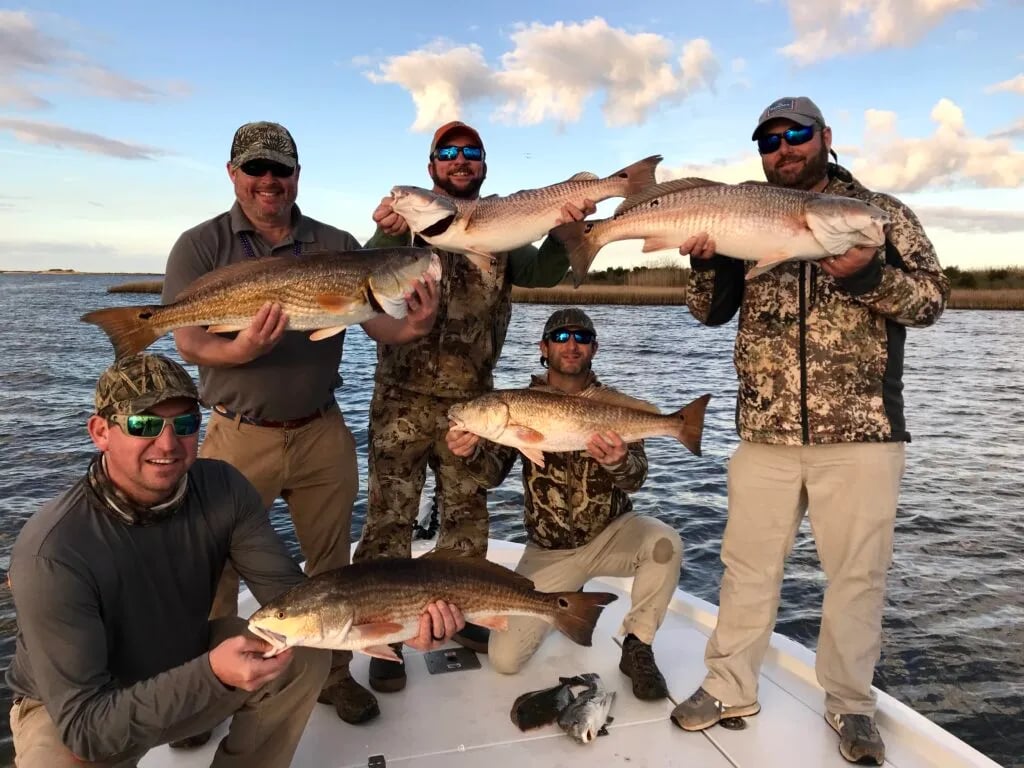 Angler smiling and holding a very large Redfish on a boat with marsh in the background.