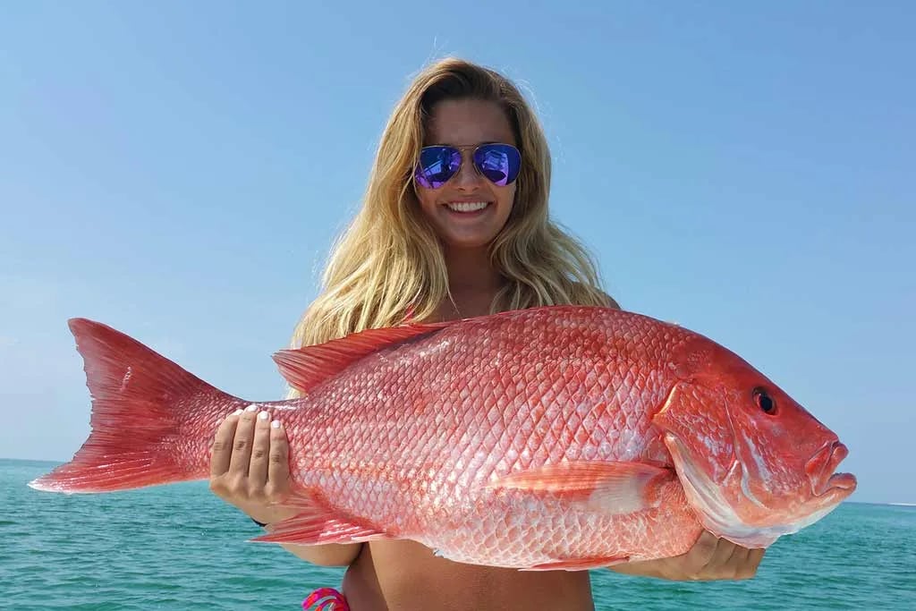 Woman in sunglasses holding a large Red Snapper against a blue sky