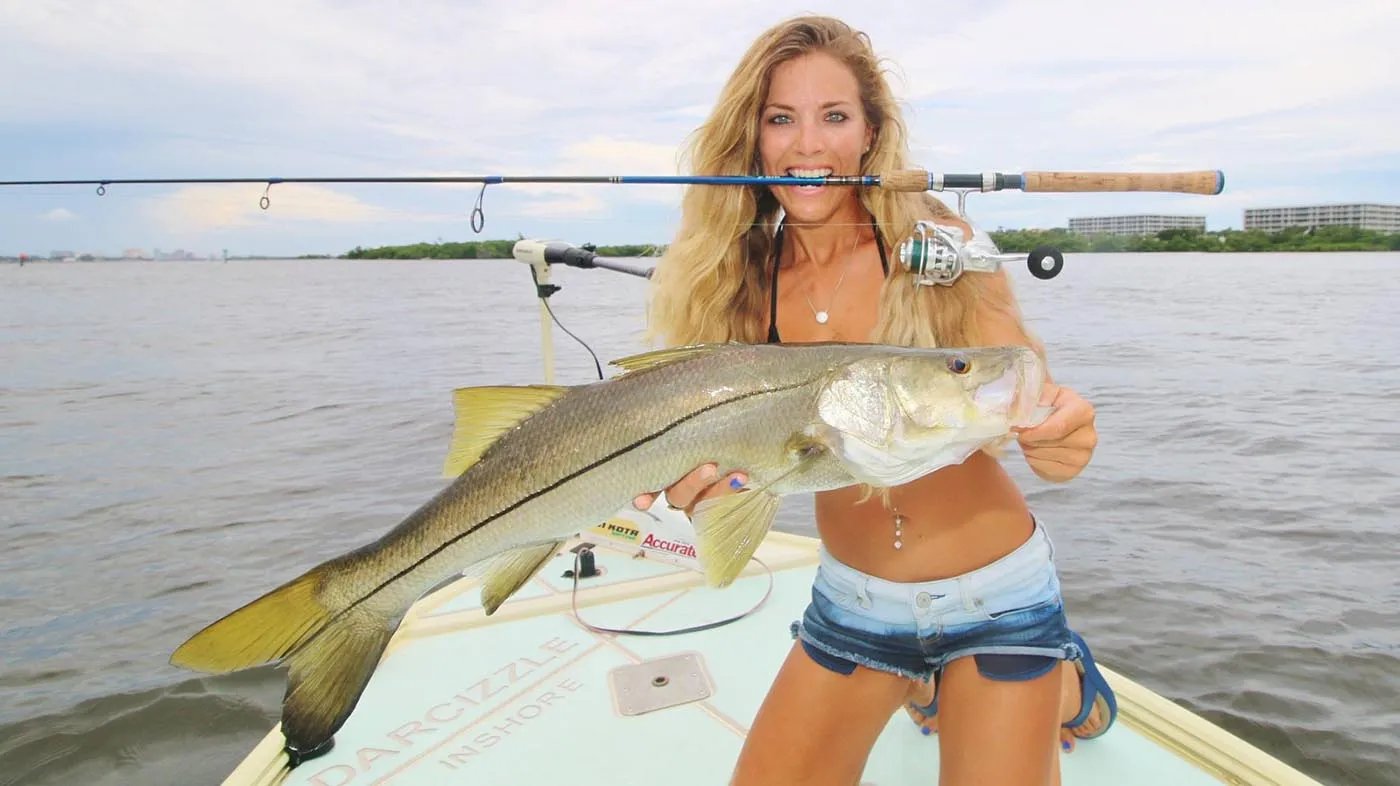 Woman holding a Snook with a fishing rod in her mouth on a boat