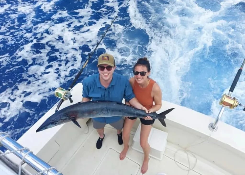 Two anglers on a boat holding a large Wahoo over the deck