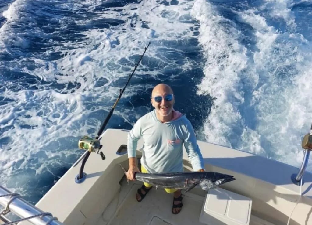 Angler on a boat holding a Wahoo with boat wake in the background