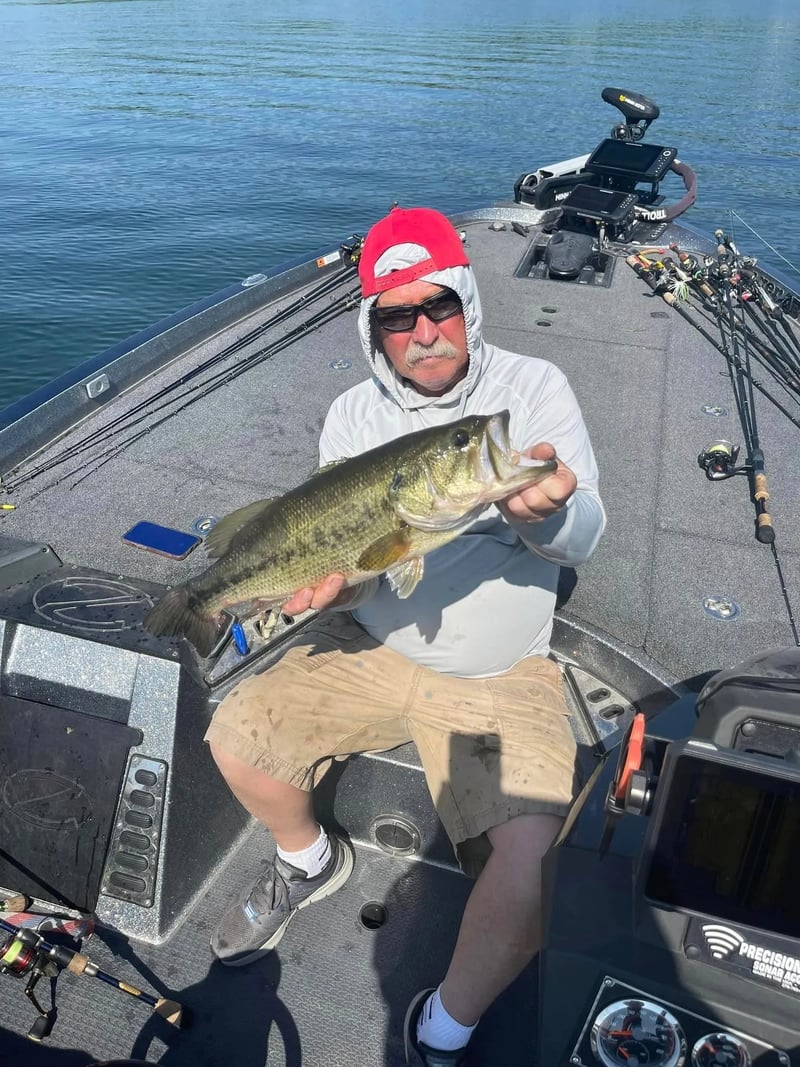 Group of six anglers on a boat, one holding a largemouth bass under a cloudy sky