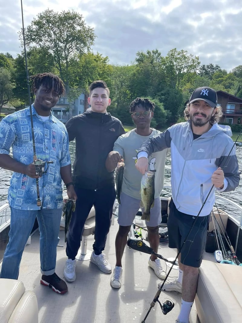 Man in a red cap and sunglasses holding a largemouth bass on a boat