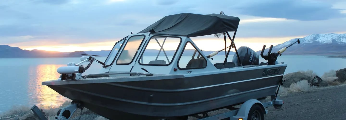 Fishing boat on a trailer at dusk by a calm lake with mountains in the distance